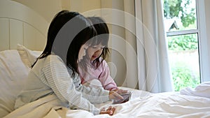 Asian sibling girls in pajamas playing the game on smartphone on a bed. mobile addiction technology concept.
