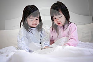 Asian sibling girls in pajamas watching smartphone on a bed at night. mobile addiction technology concept