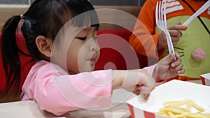 Asian sibling little girls enjoying with eating fried chicken, French fries and nectar in service shop with her family. KFC is a W