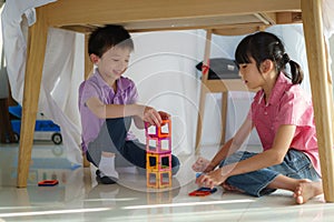 Asian sibling playing building block while sitting in a blanket fort in living room at home for perfect hideout away from their