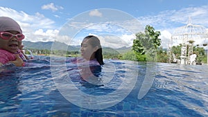 Asian sibling sisters playing in swimming pool with family in a hot summer day. Family lifestyle in vacation.