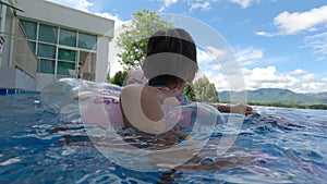 Asian sibling sisters playing in swimming pool with family in a hot summer day. Family lifestyle in vacation.