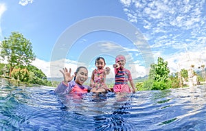 Asian sibling sisters playing in swimming pool with family in a hot summer day. Family lifestyle in vacation