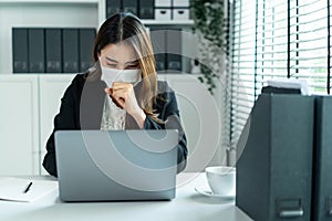 Asian sick businesswoman in formal wear facemask and work at workplace. Attractive female employee office worker coughing while