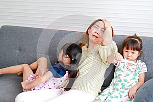 An Asian single mom is having a headache with her two young daughters sitting on the sofa