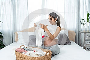 Asian single mother with big belly is about to give birth preparing clothes for her new baby. woman sits on the bed folding