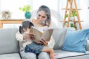 Asian single mothers have to take care of their children alone. read book to daughter. A woman sits on sofa in the living room