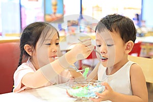 Asian sister and her little brother eating icecream together. Child girl feeding ice cream for baby boy in cafe