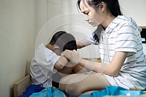 Asian sister touching shoulder,holding hand,comforting and caring for her little brother,depressed kid boy sitting and crying on