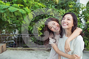 Asian sisters hugging and smiling in the park.