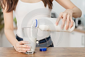 Asian slim young woman, girl pouring of fresh, dairy milk from bottle into glass or cup, drinking and eating breakfast in morning