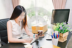 Asian small business owner work at home office, using mobile phone call, writing confirm purchase order on notebook photo