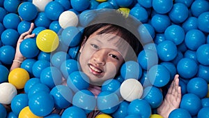 Asian smiling child girl playing lying in colorful balls park playground.16:9 style