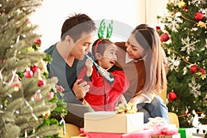 Asian smiling daughter happy teased the father and mother. My dad, mom and baby in Santa hats sitting on a couch at home near the