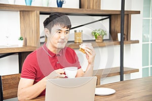 Asian smiling young man with casual  red t-shirt enjoy having breakfast, Young man cooking food and drink in the kitchen