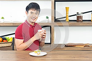 Asian smiling young man with casual red t-shirt enjoy having breakfast, eating sandwich, Young man cooking food in kitchen