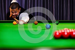 Asian snooker player while aiming to white ball shoot to hit the red ball group set in game on table