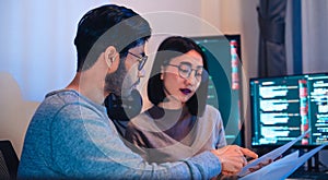 Asian software developers teams working on multiple screens displaying code and application diagrams at night in modern office