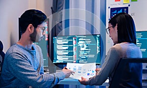 Asian software developers teams working on multiple screens displaying code and application diagrams at night in modern office
