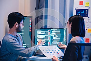Asian software developers teams working on multiple screens displaying code and application diagrams at night in modern office