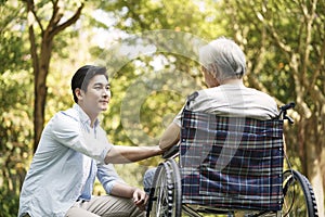 Asian son comforting wheelchair bound father