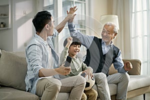 Asian son father grandfather watching soccer game on TV together at home