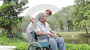 Asian son taking father in wheelchair Take a walk in the fresh air in an outdoor park.