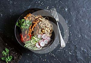 Asian spicy fried chicken in a spicy sauce with noodles and fresh vegetables on dark background