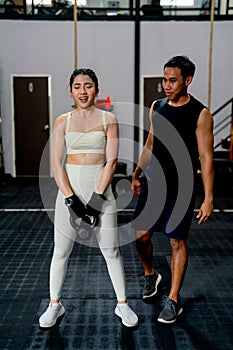 Asian sport woman hold weight to exercise with support by the trainer in fitness gym