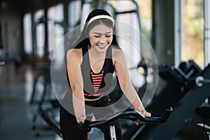 Asian sportswoman exercising on a bicycle in the gym, determination to cardio lose weight, makes her healthy. exercise bike woman