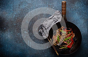 Asian stir fry noodles with vegetables in black wok pan copy space