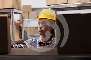 Asian storehouse worker taking cardboard box from shelf