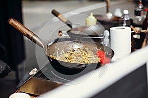 Asian street food festival in city. Chef cooking noodles and vegetables in a pan on fire. Fried chinese japanese noodles with