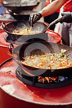 Asian street food festival in city. Chef cooking noodles and vegetables in a pan on fire. Fried chinese japanese noodles with