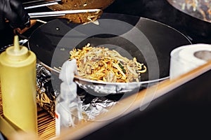 Asian street food festival in city. Chef cooking noodles and vegetables in a pan on fire. Fried chinese japanese noodles with