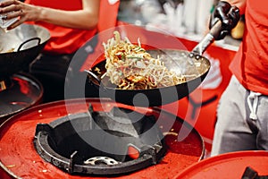 Asian street food festival in city. Chef cooking noodles and vegetables in a pan on fire. Fried chinese japanese noodles with