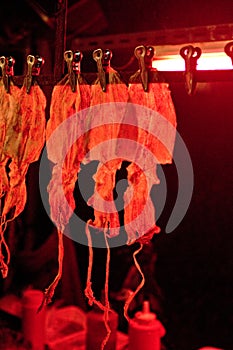 asian street food: row of dried Grilled squid clipped on the rope in red light for sale on night market