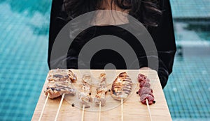 Asian Street Food. Woman holding tray of Grilled Chicken, Meat and Pork