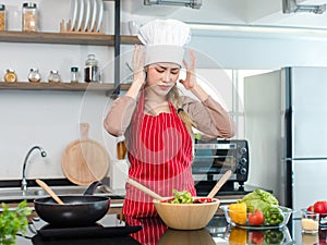 Asian stressed depressed worried female frowning face chef housewife wears white tall cook hat apron standing holding hands on