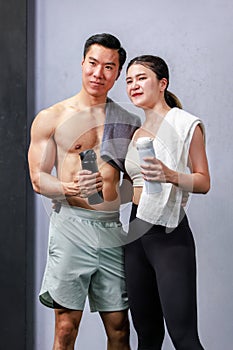 Asian strong fit young male muscular shirtless fitness model in sporty shorts and female athlete in sport bra standing smiling