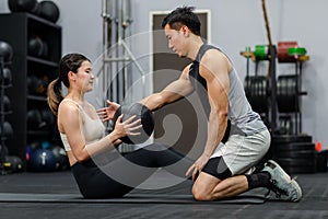 Asian strong young male muscular fitness trainer helping female athlete model in sexy sport bra and legging lifting working out