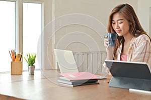 Asian student girl holding a coffee cup and using a laptop is working on a project to finish her studies