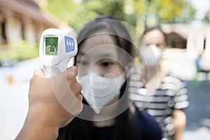 Asian student girl wear medical face mask is checking fever outside of school during its reopening after COVID-19 lockdown,screen