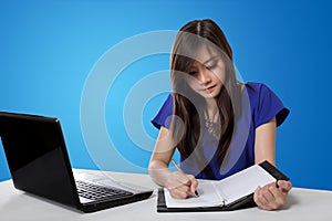 Asian student girl writing on notebook, on blue background