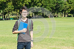 Asian student holding books and smiling while standing in park a