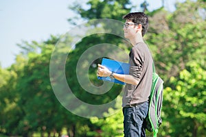 Asian student holding books and smiling while standing in park a