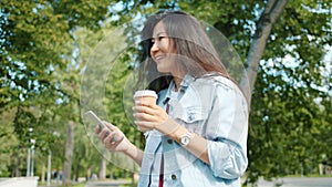 Asian student walking in park using smart phone drinking to go coffee smiling