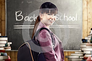 Asian student woman with backpack standing and look back in the classroom with piles of books and blackboard