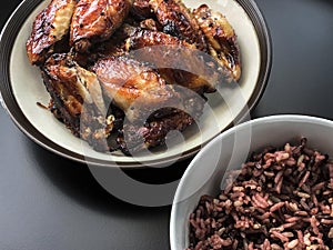 Asian style air fried chicken wings with ceramic dish serve with small bowl of cooked Rice berry. On black background.
