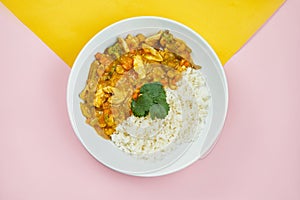 Asian style dish - Chicken Curry with Rice Served Vegetables in a white bowl on colored backgrounds. Minimalistic food. Top view